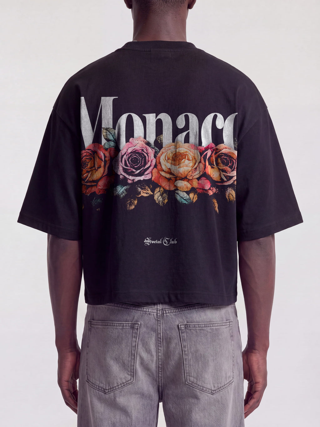 Black Bloom boxy tee on model, back view with white Monaco wordmark over faded roses.