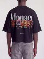 Black Bloom boxy tee on model, back view with white Monaco wordmark over faded roses.