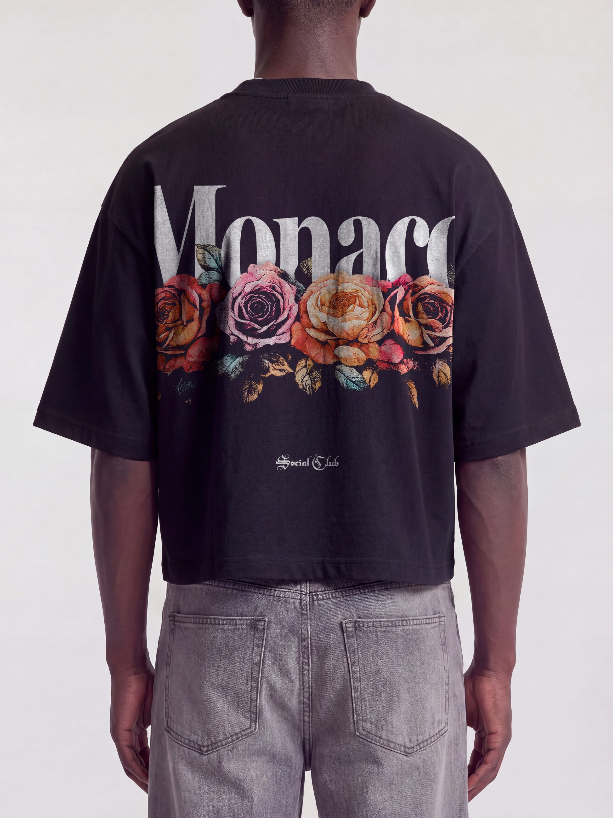 Black Bloom boxy tee on model, back view with white Monaco wordmark over faded roses.