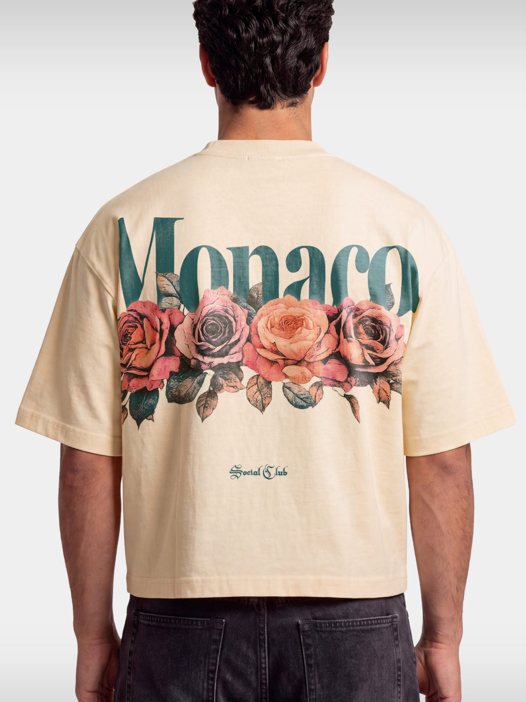 Monaco Bloom ivory boxy tee worn by model, back view with teal wordmark and rose graphic.