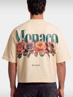 Monaco Bloom ivory boxy tee worn by model, back view with teal wordmark and rose graphic.