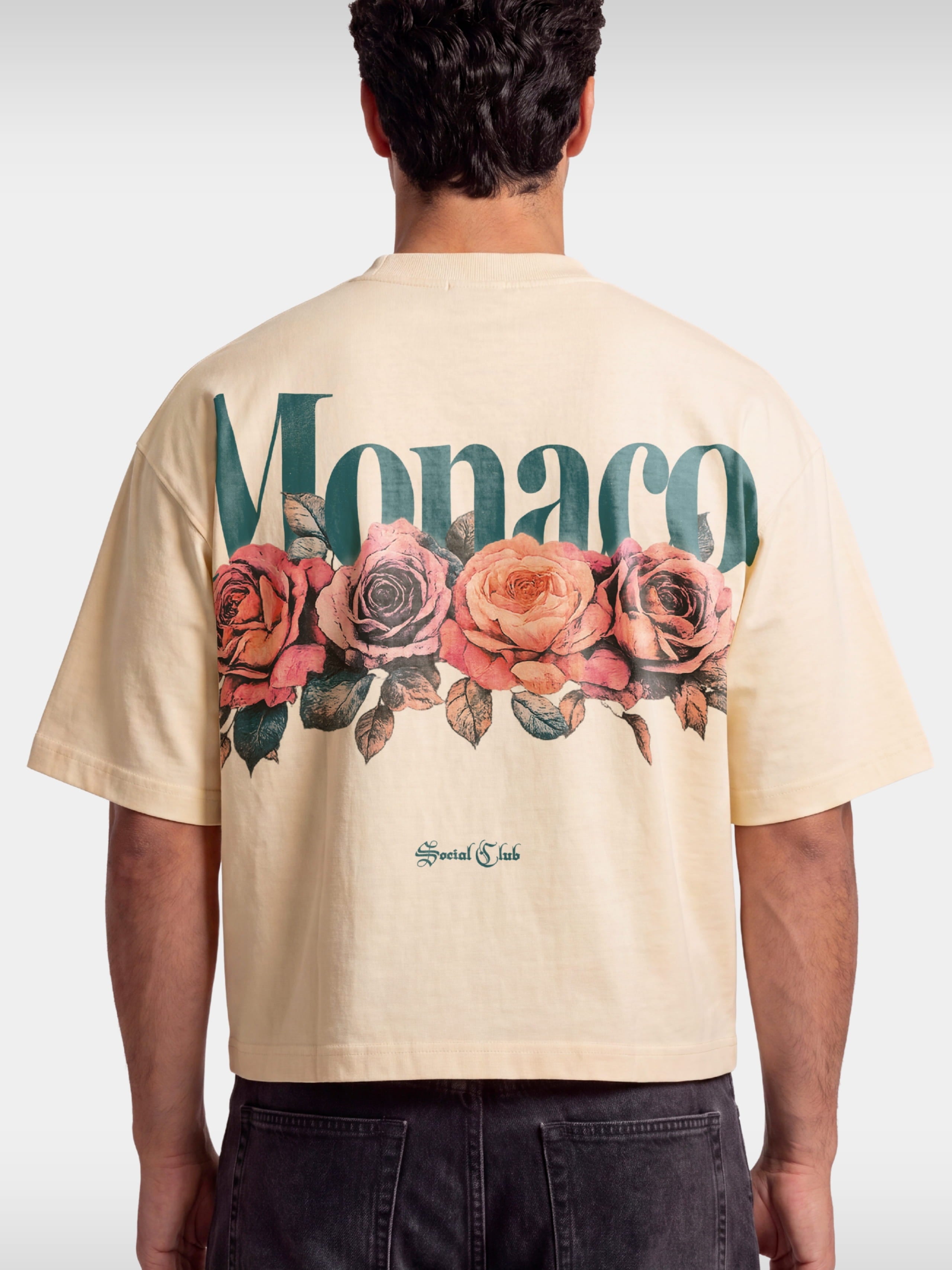 Monaco Bloom ivory boxy tee worn by model, back view with teal wordmark and rose graphic.