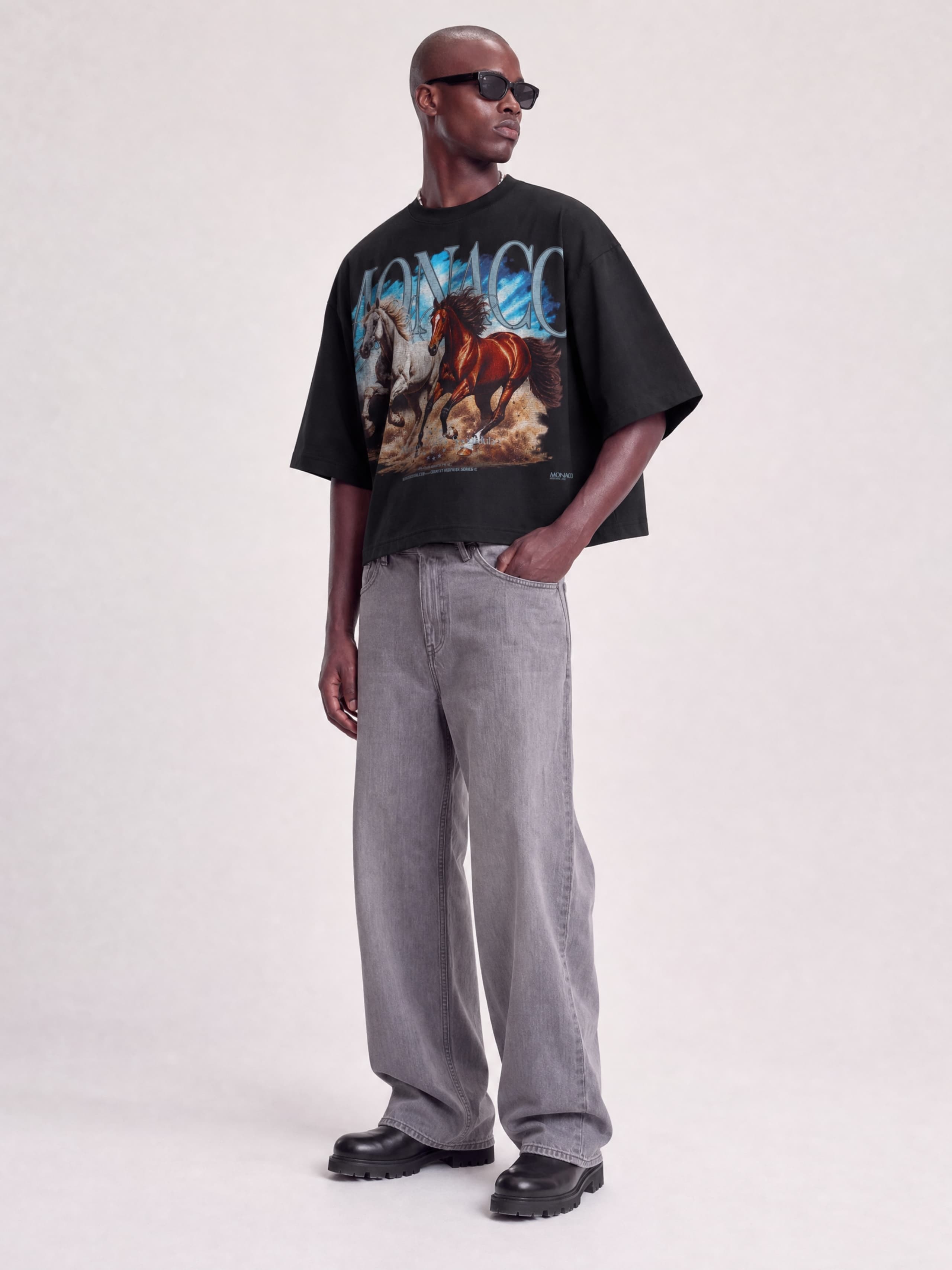 Full-length view of model in Monaco Run Wild black boxy tee with horse graphic and MONACO arch.