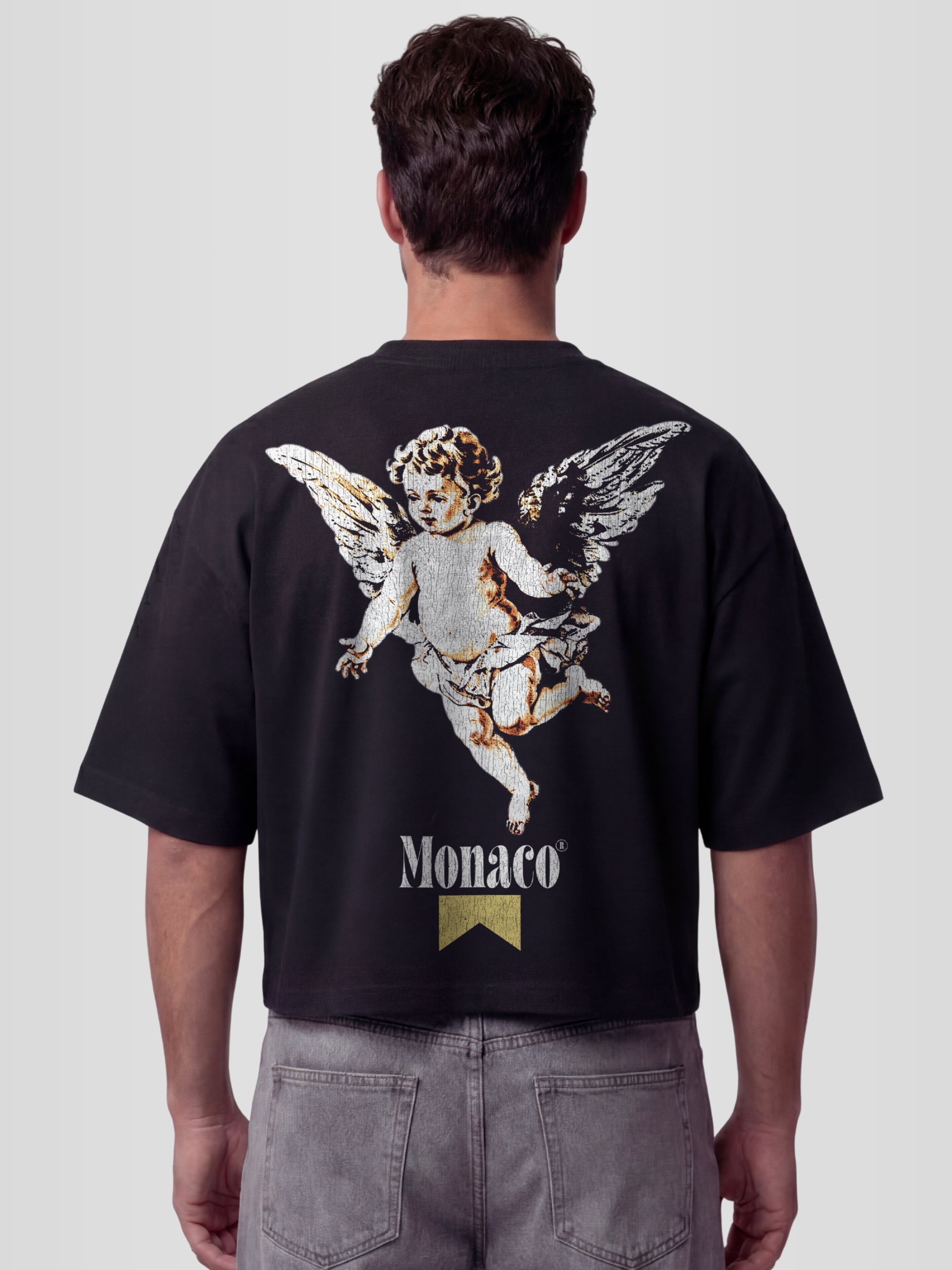Man model wearing The Cherub Heavyweight Boxy Tee in Black with single angel and Monaco gold ribbon graphic — Monaco Social Club streetwear