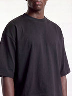 Black boxy tee on model, cropped front view showing ribbed crew neck and drop shoulders.